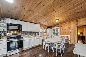 A kitchen with white cabinets, a black microwave, stainless steel appliances, and a dining area with white chairs and a table.