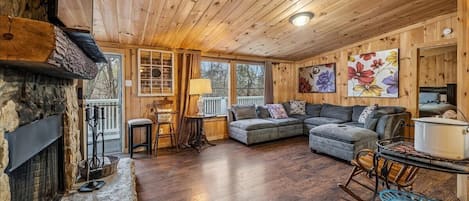 A cozy cabin interior with a stone fireplace, wooden ceiling, and a living area featuring a sofa and a dining table.