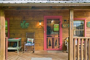 Eine Holzhütte mit roter Tür, einer kleinen Veranda mit Stuhl und Tisch und einem Willkommensschild.