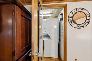 Una puerta de madera que da a un cuarto con un electrodoméstico blanco y un espejo decorativo en la pared.