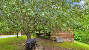 A tree-lined outdoor area with a covered object, a brick wall, and a utility box. - Serene Cozy Cabin w/ Hot Tub & Games (Sevierville)