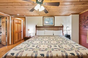 A bedroom with a wooden ceiling, a bed with a quilt, a nightstand, a lamp, and a door. - Serene Cozy Cabin w/ Hot Tub & Games (Sevierville)