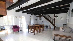 A spacious living area with a wooden dining table, a purple armchair, and a staircase leading to an upper floor.