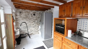 A compact kitchen with a stone wall, wooden cabinets, a built-in oven, and a washing machine.