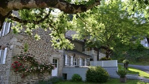 A stone building with a balcony, surrounded by lush greenery and a well-maintained lawn.