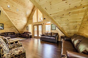 An attic-style room with wooden walls and a sloped ceiling. It features two leather sofas, a patterned armchair, and a wooden coffee table. - 15‑Bedroom Lodge with Arcade & Theater (Sevierville)