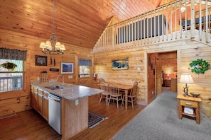 A wooden cabin interior with a kitchen, dining area, and a loft bedroom. - Mountain Cabin w/ Hot Tub & Fireplace (Sevierville)