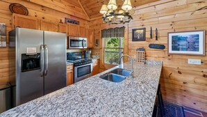 A kitchen with wooden walls, granite countertops, stainless steel appliances, and a hanging light fixture. - Mountain Cabin w/ Hot Tub & Fireplace (Sevierville)
