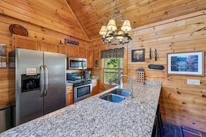 A kitchen with wooden walls, granite countertops, stainless steel appliances, and a hanging light fixture. - Mountain Cabin w/ Hot Tub & Fireplace (Sevierville)