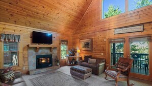 A cozy log cabin interior with a stone fireplace, leather furniture, and a television. - Mountain Cabin w/ Hot Tub & Fireplace (Sevierville)