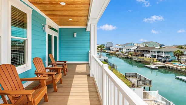 Een balkon met houten stoelen, uitzicht op een jachthaven met boten en huizen op de achtergrond.