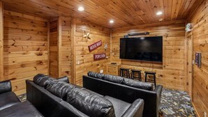 Um quarto acolhedor com paredes de madeira, televisão de tela plana, sofás de couro e um letreiro com a inscrição 'pipoca'.