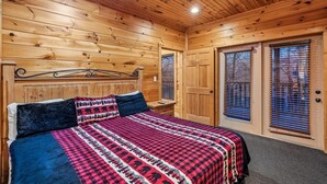 Quarto com painéis de madeira, uma cama, duas mesas de cabeceira e uma porta com persianas.