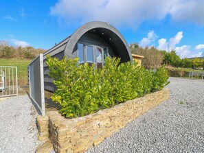 A modern, curved-roofed building with a stone wall and gravel driveway.