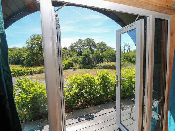 A view through a glass door onto a wooden deck with a garden in the background.