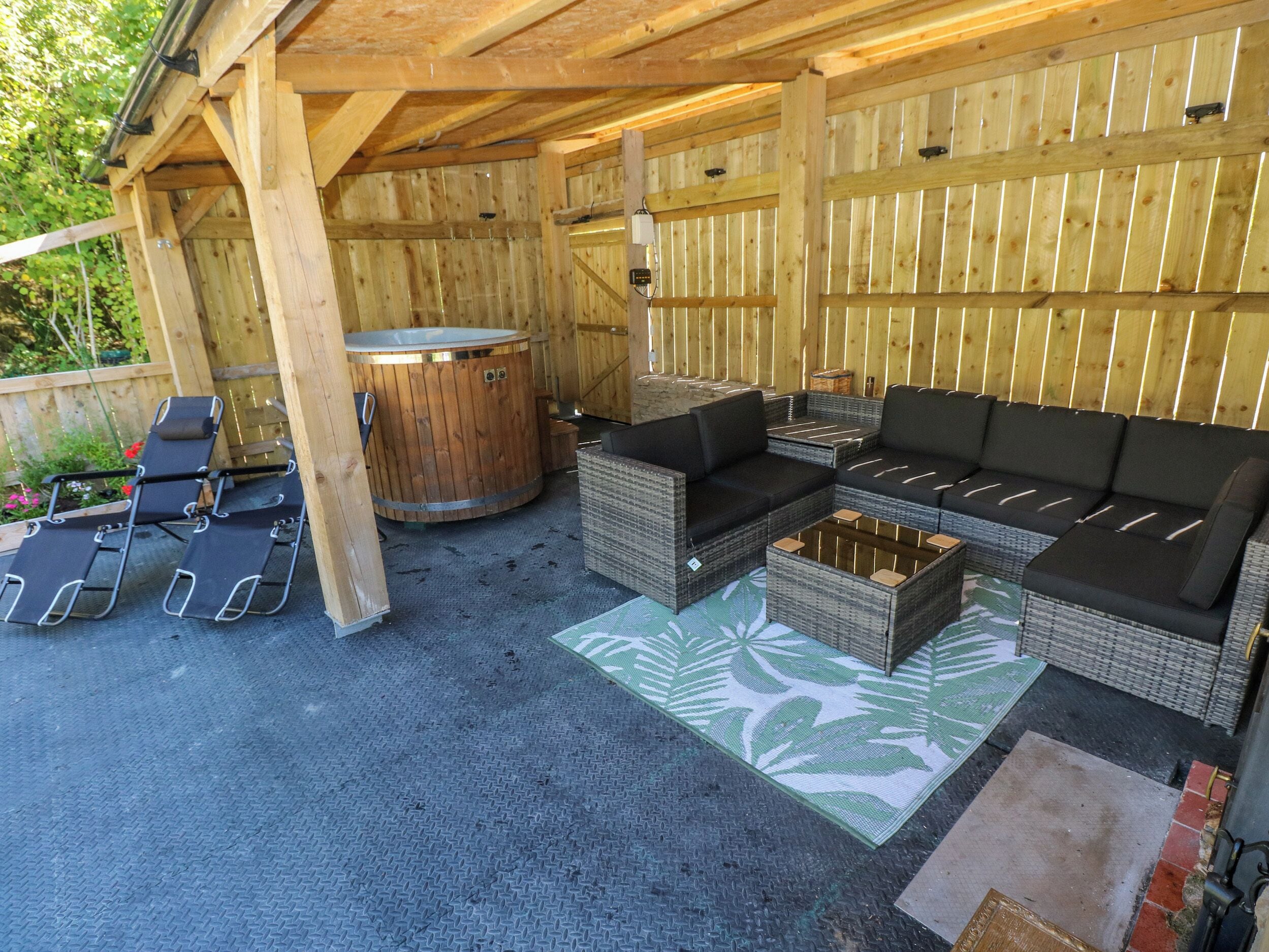 An outdoor patio with a wooden pergola, a hot tub, lounge chairs, and a sofa.
