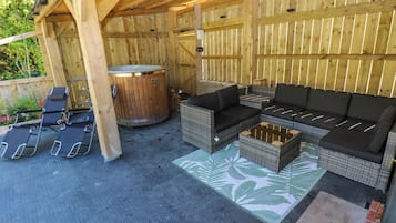 An outdoor patio with a wooden pergola, a hot tub, lounge chairs, and a sofa.