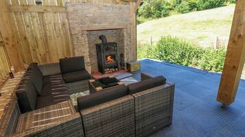 A covered outdoor seating area with a stone fireplace and a view of the outdoors.
