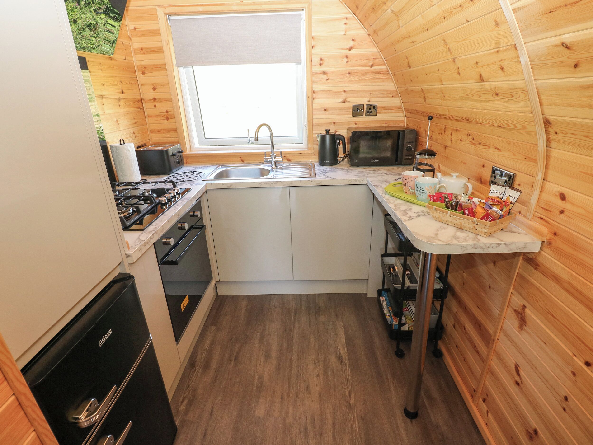 A compact kitchen with a sink, stove, microwave, and a window above the sink.