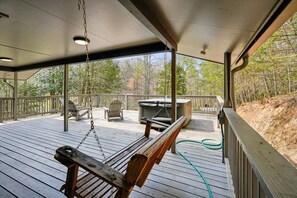 A covered outdoor deck with a swing, chairs, and a hot tub. - Wooded Family Retreat w/ Hot Tub & Games (Gatlinburg)