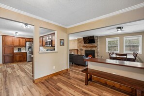 A spacious living area with a fireplace, a dining table, and a kitchen in the background. - Wooded Family Retreat w/ Hot Tub & Games (Gatlinburg)