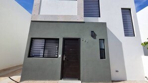 A modern two-story building with a flat roof, a central entrance with a black door, and a small overhang above the door. - 3 Bedroom home in Gated Community (La Paz)