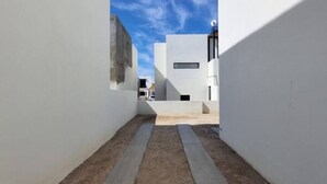 A narrow alleyway with concrete pathways and white walls, leading to a building with a flat roof and a satellite dish. - 3 Bedroom home in Gated Community (La Paz)