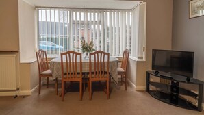 A dining area with a round table, four chairs, a vase with flowers, and a television on a stand. - No 48 - 3 Bedroom Heworth in York (York)