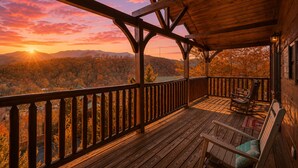 Eine Holzterrasse mit Blick auf einen Sonnenuntergang über einer bewaldeten Landschaft.