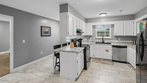 A kitchen with white cabinets, a granite countertop, and a stainless steel refrigerator. - 4BR Home | Theater + Hot tub + Games + Fire Pit (Gatlinburg)