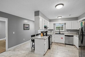 A kitchen with white cabinets, a granite countertop, and a stainless steel refrigerator. - 4BR Home | Theater + Hot tub + Games + Fire Pit (Gatlinburg)