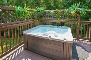 A hot tub on a wooden deck with a lattice fence and greenery in the background. - 4BR Home | Theater + Hot tub + Games + Fire Pit (Gatlinburg)