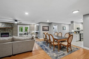 A modern living room with a sofa, dining table, and chairs. There is a kitchen area with cabinets and appliances. - 4BR Home | Theater + Hot tub + Games + Fire Pit (Gatlinburg)