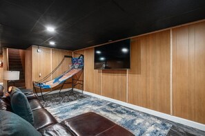 A room with a hammock, a TV mounted on the wall, a leather couch, and a patterned rug. - 4BR Home | Theater + Hot tub + Games + Fire Pit (Gatlinburg)