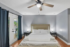 Ein Schlafzimmer mit einem Bett, Deckenventilator, zwei Nachttischen und Blick durch eine Glastür.