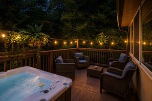 An outdoor deck with a hot tub, wicker furniture, and string lights. - 4BR Home | Theater + Hot tub + Games + Fire Pit (Gatlinburg)