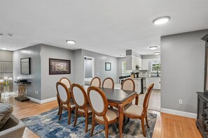 A dining area with a table and chairs, a kitchen in the background, and a living room with a sofa. - 4BR Home | Theater + Hot tub + Games + Fire Pit (Gatlinburg)