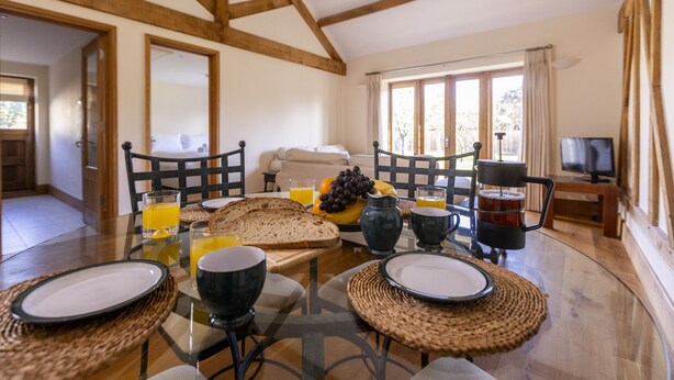 Una escena de desayuno con una mesa para dos, incluyendo platos, tazas y un frutero con plátanos y uvas.