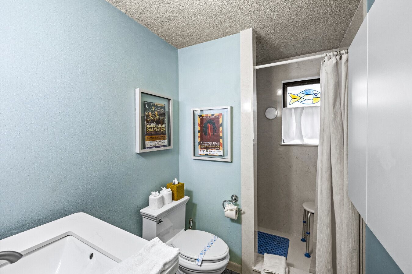 Un baño con inodoro, lavamanos y ducha. Hay dos carteles enmarcados en la pared.