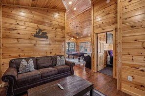 Ein Holzblockhaus-Innenraum mit einer Couch, einem Billardtisch und einem Deckenventilator.