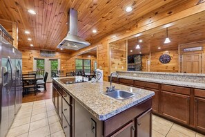 Ein Holzhütten-Interieur mit einer Küche, die sich durch Granit-Arbeitsplatten, eine Edelstahl-Spüle und einen Kamin aus Naturstein auszeichnet.