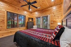 Una camera da letto in una baita di legno, con un letto, una ventola a soffitto e un televisore.