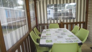 Een overdekt terras met een eettafel en stoelen, houten leuningen en ramen met uitzicht op huizen.