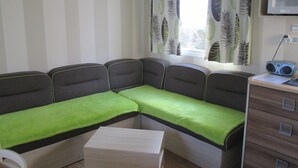 Een compacte kamer met een bank, een klein tafeltje, een kast en gordijnen met een bladmotief.