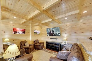 Ein gemütliches Blockhaus-Interieur mit Kamin, Ledersitzgelegenheiten und einem an der Wand montierten Flachbildfernseher.
