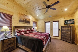 Ein Schlafzimmer mit Bett, Holzwänden, Deckenventilator, Fernseher und Kommode.