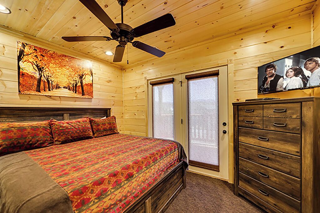 A bedroom with a bed, a ceiling fan, a dresser, and a television.