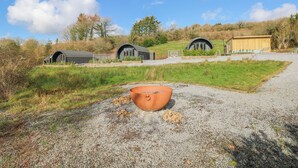 Un paysage rural avec trois bâtiments modernes aux toits incurvés, un chemin de gravier et un grand pot en terre cuite au premier plan.