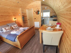 Una cabana de fusta acollidora amb un llit, una taula de dinar per a dues persones i una cuineta.