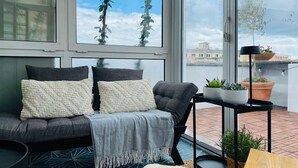Ett modernt vardagsrum med en grå soffa, två kuddar, en pläd och ett svart sidobord med krukväxter.